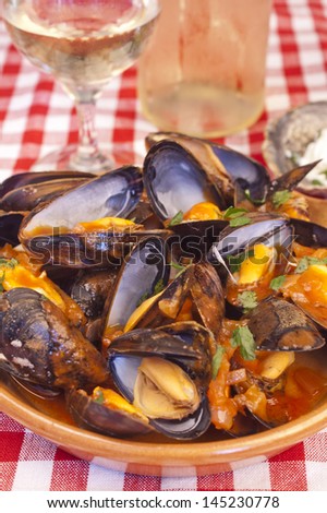 Plate of steamed mussels with tomato and white wine sauce or marinara sauce and with a glass and a bottle of white wine in the background