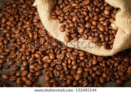 Coffee beans in coffee bag made from burlap on wooden surface.