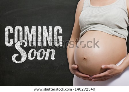 pregnant woman in front a chalkboard with coming soon text