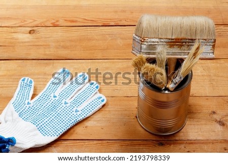A brush for applying paint, glue, varnish or other materials to various surfaces. Brush with wooden handle and stiff bristles. Iron can with paint or varnish. And a work glove And a work glove ストックフォト © 