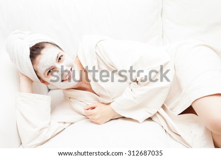 Young Woman in Bathrobe with Facial Beauty Mask Laying on a Sofa