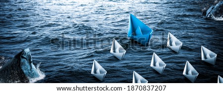 
Blue Paper Boat Leading A Fleet Of Small White Boats Around Rocks In Rough Water - Leadership Concept