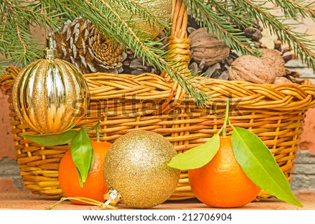 Golden Christmas balls and tangerines on a background of a basket with pine cones and walnuts and green spruce branches