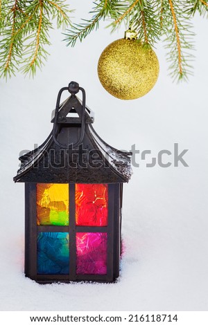 Multicolored decorative lantern in the snow and fur-tree branch with  Christmas ball