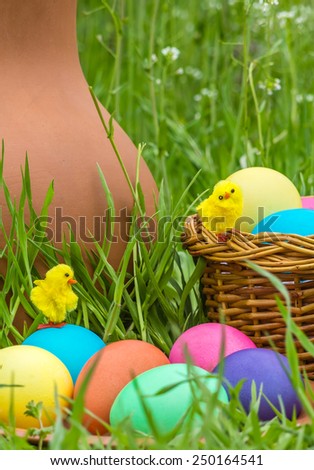Painted Easter eggs and toy chickens on the background of a clay pitcher and green spring grass