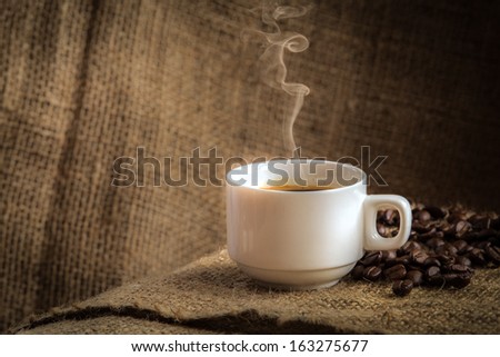 Coffee cup and white smoke on sack cloth. Dark background.