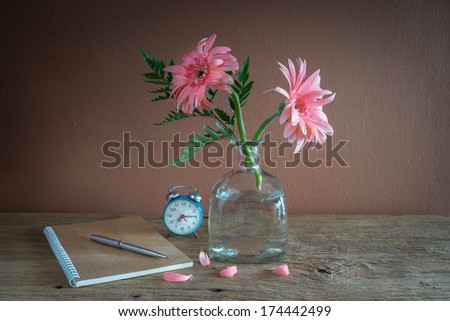 Still life with pink flowers in bottle, alarm clock and note book
