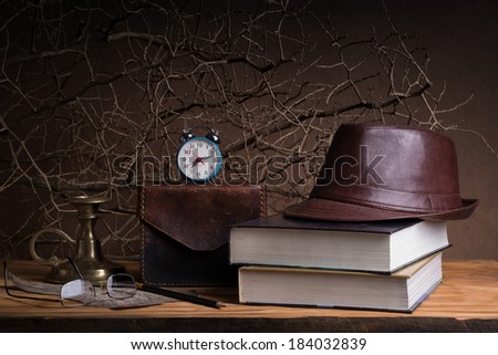 Still life with vintage leather hat on books, leather case brass candlestick and glasses