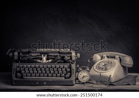 still life with old typewriter, telephone, alarm clock and glasses on wooden table