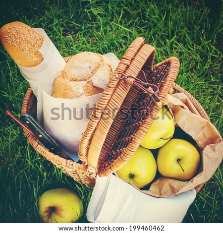 Picnic Food in a Wattled Basket on Green Grass, Fresh Bread, Apples. Image with filter effect instagram