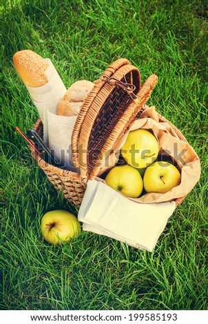 Picnic Wattled Basket with Fresh Bread, Apples and cheese on Green Grass, vertical image