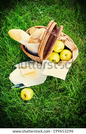 Picnic Wattled Basket with Fresh Bread, Apples and  cheese on Green Grass