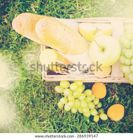 Wattled Basket with Fresh Bread, Apples, Fruit on Green Grass, Picnic. Square image with toned, instagram effect