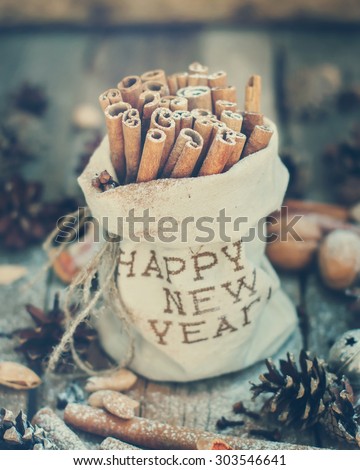 Linen Bag with Embroidery Happy New Year with Sticks of Cinnamon and  other Christmas Ingredients, Pine cones, Walnuts on Wooden Background. Toned Vintage Christmas Composition