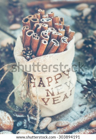 Sticks of Cinnamon in a linen Bag Embroidered with Happy New Year on Christmas Table, other christmas ingredients, Pine cones, Walnuts. Toned