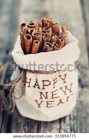 Linen Bag with Embroidery Happy New Year with Sticks of Cinnamon on Wooden Background. Toned Vintage Christmas Composition with selective focus