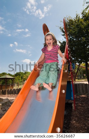 Cheerful little girl having fun while sliding down on the slide with bursting laugh