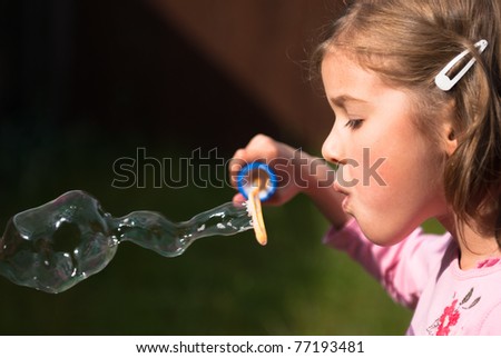 Beautiful little girl blowing an elaborate giant bubble