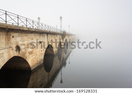Symmetrical reflection of the Roman bridge hidden in the fog