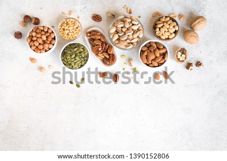 Various Nuts in  bowls on white background, top view, copy space. Nuts assortment frame - pecans, hazelnuts, walnuts, pistachios, almonds, pine nuts, peanuts, pumpkin seeds.