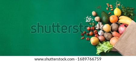 Shopping or delivery healthy food background. Healthy vegan vegetarian food in paper bag vegetables and fruits on green, copy space. Food supermarket and clean vegan eating concept.