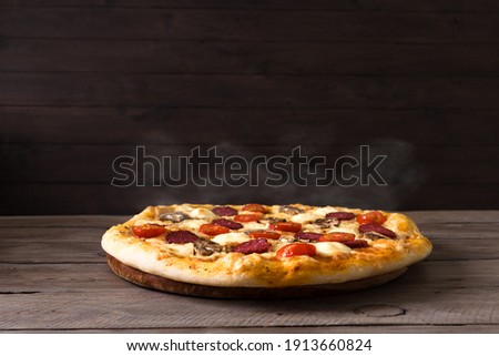 Traditional Italian Pizza with mozzarella and salami. Hot Pizza just from oven, black background, copy space. Delivery pizza or pizzeria promotional concept.