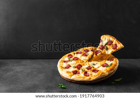 Traditional Italian Pizza with mozzarella and pepperoni or salami. Fresh slices Pizza flying over black background, copy space. Delivery pizza or pizzeria promotional concept.