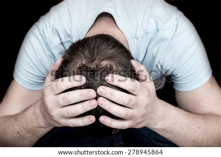 Depressed crying scared man holding his head in his hands sitting on floor over black background. Despair, depression, hopelessness, addiction concept.