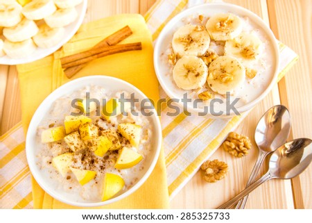 Oatmeal porridge with fruits (banana, apple) and nuts over wooden table, healthy organic breakfast