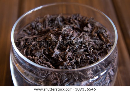 Black dry tea leaves in glass jar on wooden background