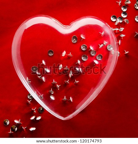 A glass heart sitting on a pile on thumb tacks