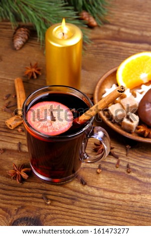 Mulled wine in glass with cinnamon stick, candle and sweets, vertical