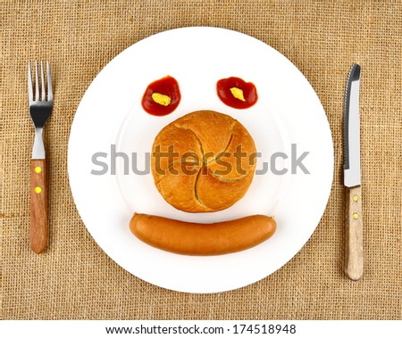 Sausage with bun on the plate as Funny Face, top view