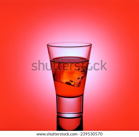 Short drink glass with red liquid and ice cubes, red background