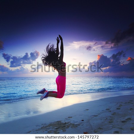 Young woman with raised hands jumping on sunset beach