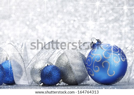 Blue shiny christmas balls and ribbon on silver glitter stars background