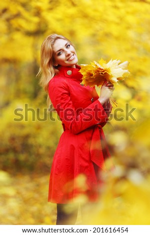 Young beautiful woman posing in autumn park with a bunch of dry leaves