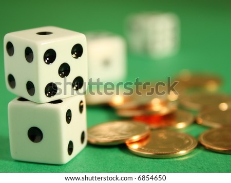 A close up on two dices on the foreground beside several coins and two dice on the background, shallow depth of field.