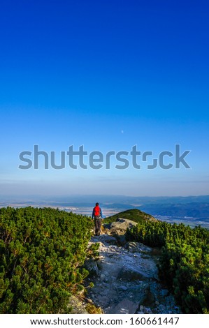Man walking forward on a mountain tourist path heading straight towards the moon. Inspirational picture.
