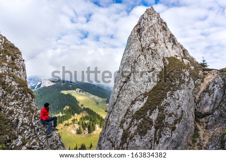 Young woman climber sitting on cliff\'s edge and looking to a sky with clouds