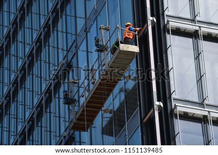 Construction workers on a suspended platform on a skyscraper glass facade Foto d'archivio © 