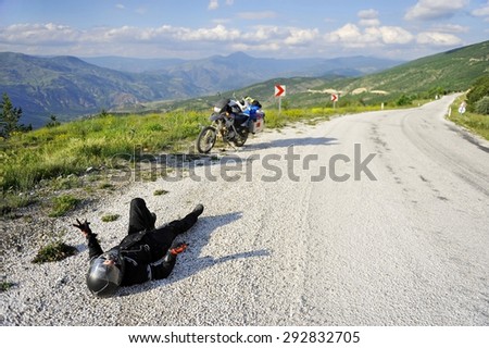 SAFRANBOLU/TURKEY - JUNE 21: Happy motorcyclist resting on the ground next to a motorcycle loaded with luggage on an empty mountain road on June 21, 2015 in Safranbolu.