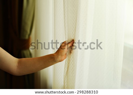 Hand pulling a window curtain for warm daylight to enter the room