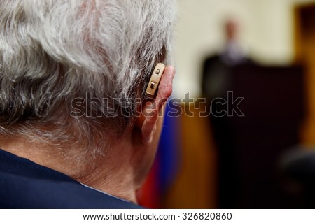 Detail shot with a hearing aid device used by old man during conference