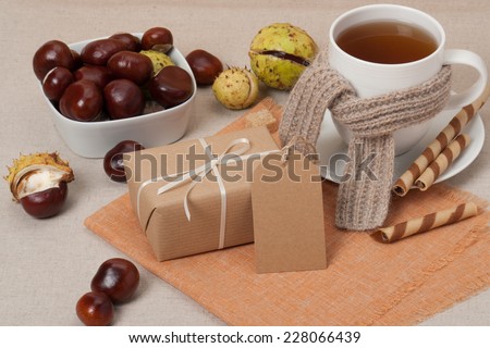 Gift Box With Blank Tag. Cup Of Hot Tea With Sweets. Chestnuts. Natural Linen Table Cloth.