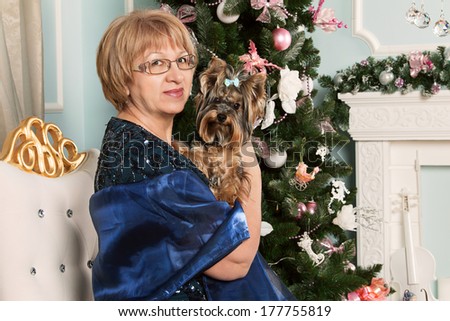 Beautiful adult woman. Keep a small dog in her arms. Spending time before trace holidays. Christmas atmosphere in the interior room. Wait until the new year. Elegant older woman sitting in a lounge.