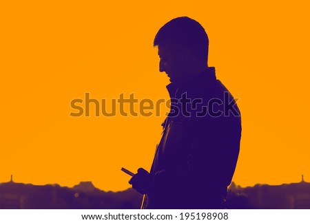 Silhouette of man standing on city background, sunset and blue sky. Man holding a telephone. Silhouette, man, sunset, city, phone - gradient advertising concept.