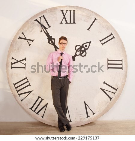Man standing near the clock. Arrows show the big clock time. Male student or office worker. The clock at five minutes to two. Time to take a break for lunch and rest.