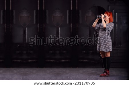 Modern woman looking through binoculars. A woman holding a pair of binoculars. Girl with binoculars in hand on background of industrial premises. Technology in search of something. The search system.