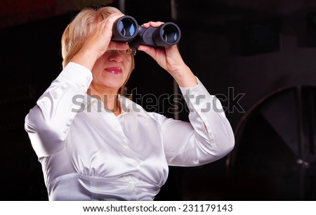 Modern adult business woman looking through binoculars. Woman in business attire holding a pair of binoculars. Watch with binoculars in search of something. Concept screen saver or insurance company.
